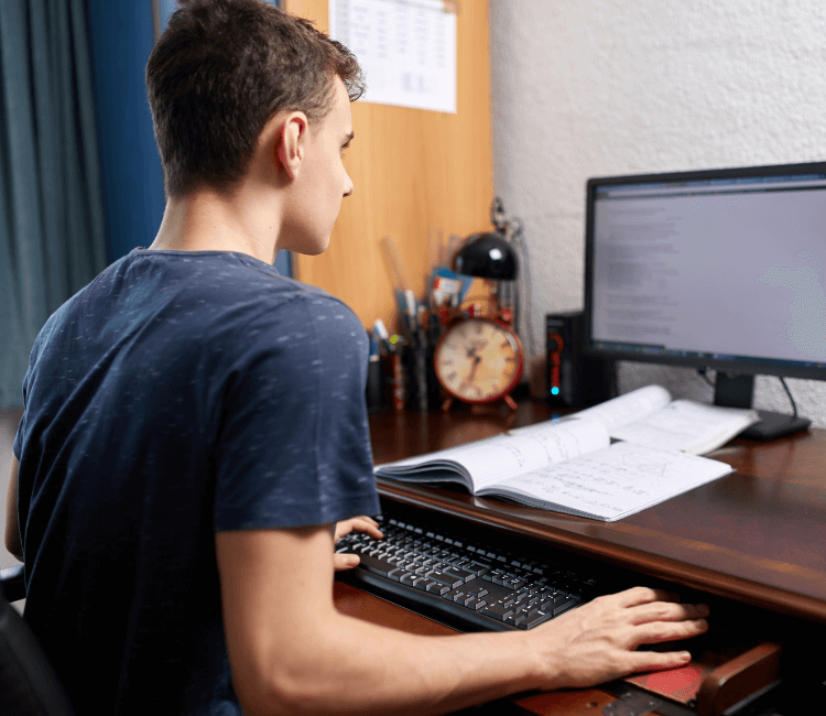 Transitioning Autistic Teens to life after high school - Image of a teenage boy sitting at his desk with a notebook and desktop computer